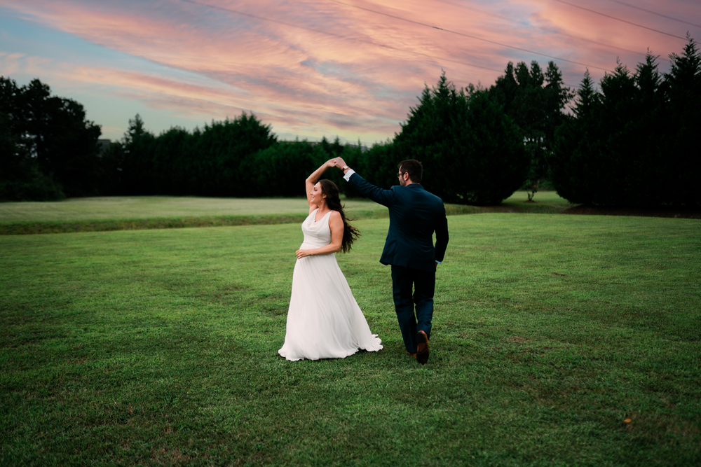 The couple walks hand in hand across the field at sunset.