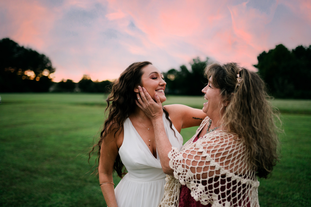 The bride laughs with a guest beneath the sunset sky.