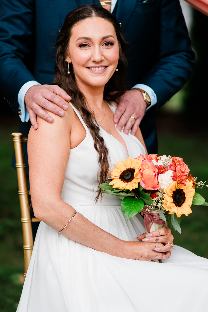 The seated bride holds her colorful bouquet with the groom behind her.