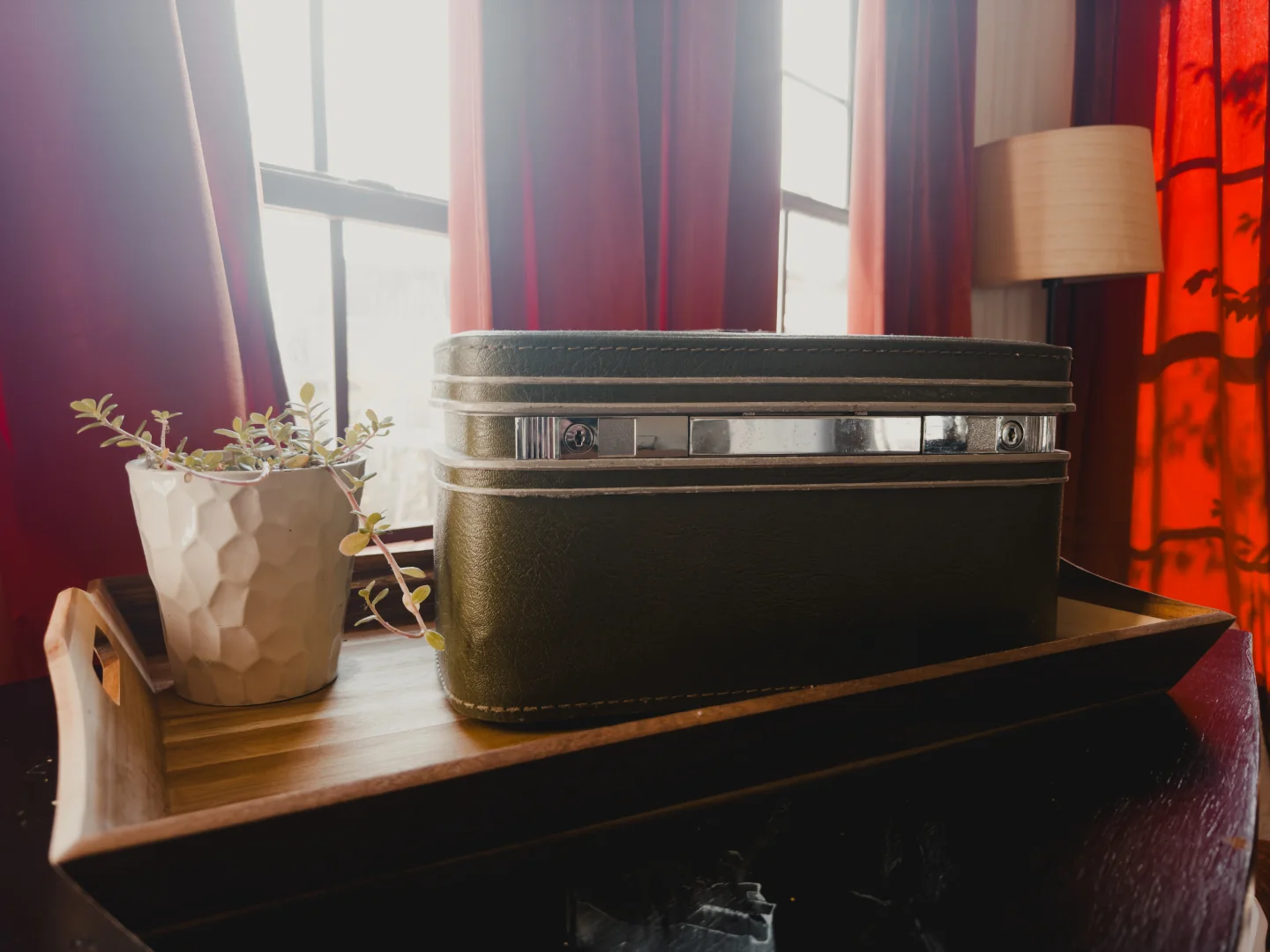 The olive-green keepsake box, closed on a wooden tray beside a plant and sunlit curtains.