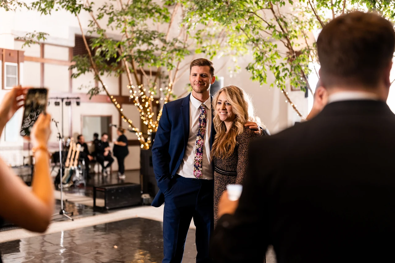 Smiling reception guests framed by other guests in an indoor courtyard.