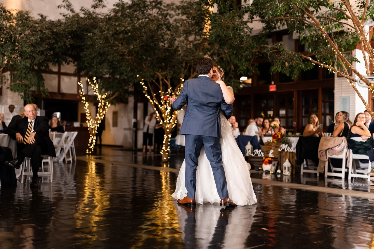 Newlyweds dance on a reflective dark floor among reception guests.