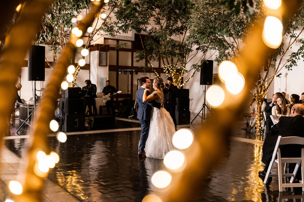 Newlyweds dance between glowing foreground string lights.