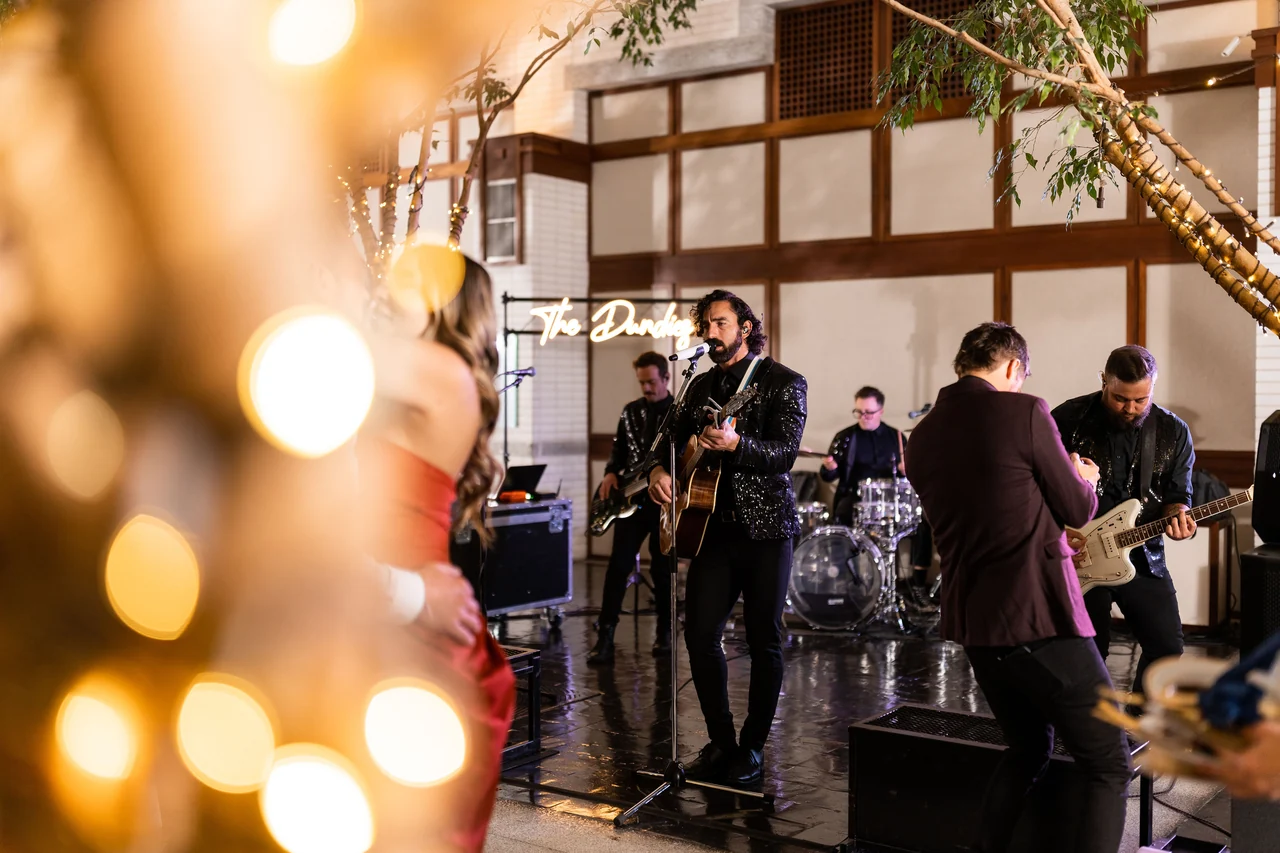 A live band performs through glowing foreground string lights.