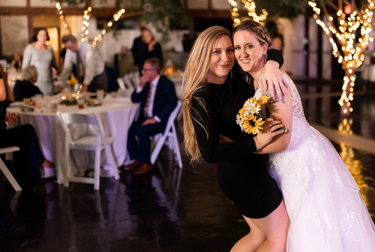 Bride poses with a guest holding sunflowers at the reception.