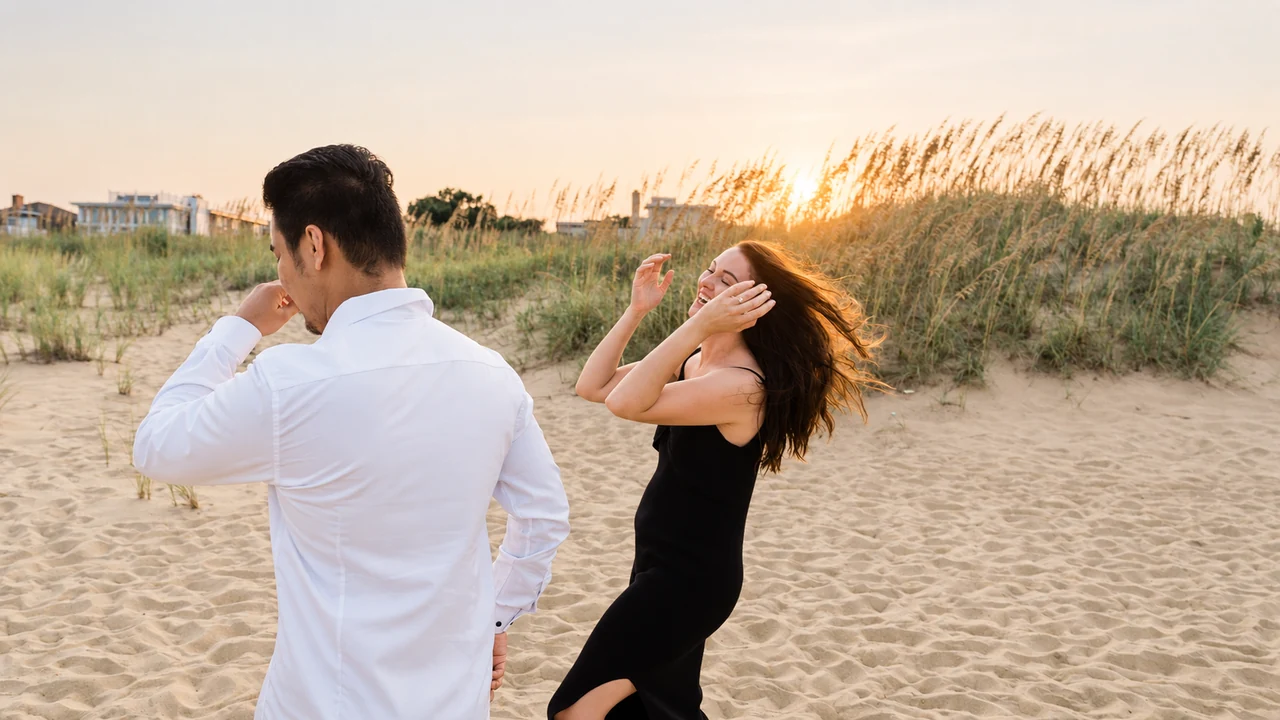 Couple laughs and dances beside beach grasses at sunset.