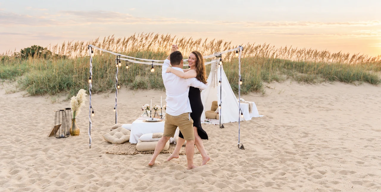 Couple dances in front of a styled beach picnic and canopy at sunset.