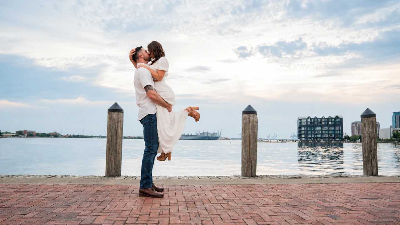 Couple embraces with her lifted off the ground on a brick waterfront promenade.