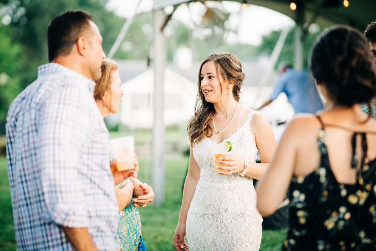 Bride smiles with a drink while talking with guests.