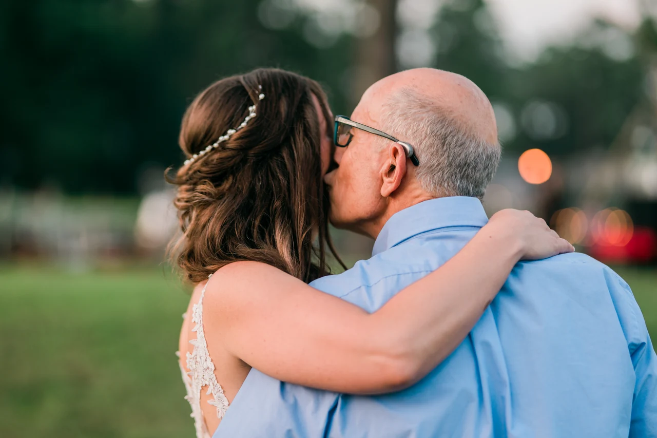 Bride embraces an older male guest outdoors.