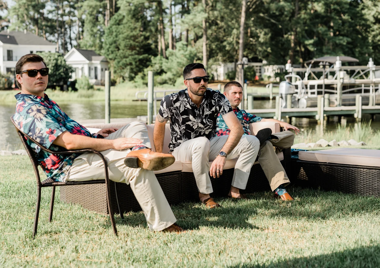 Groom and groomsmen relax in chairs by the water.
