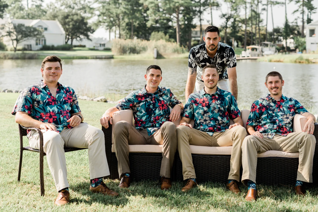 Groom and four groomsmen pose around an outdoor couch beside the water.