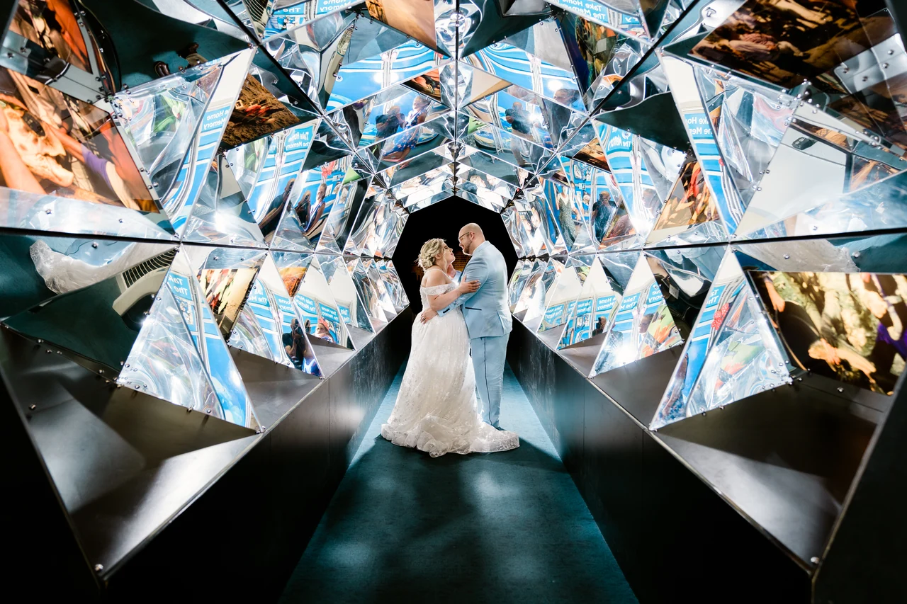 Bride and groom embrace within an angular mirrored installation.